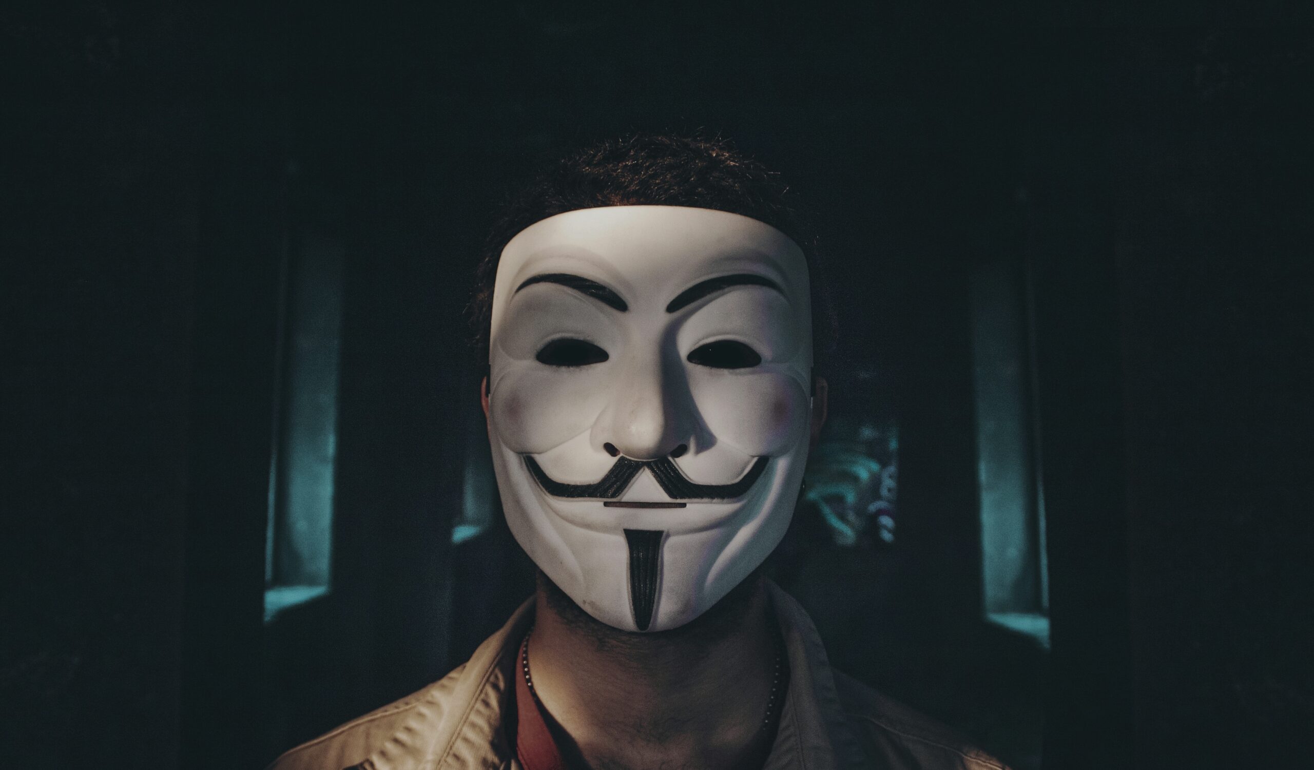 Osoba chcąca zachować anonimowość w sieci, w masce Guya Fawkesa na ciemnym tle.