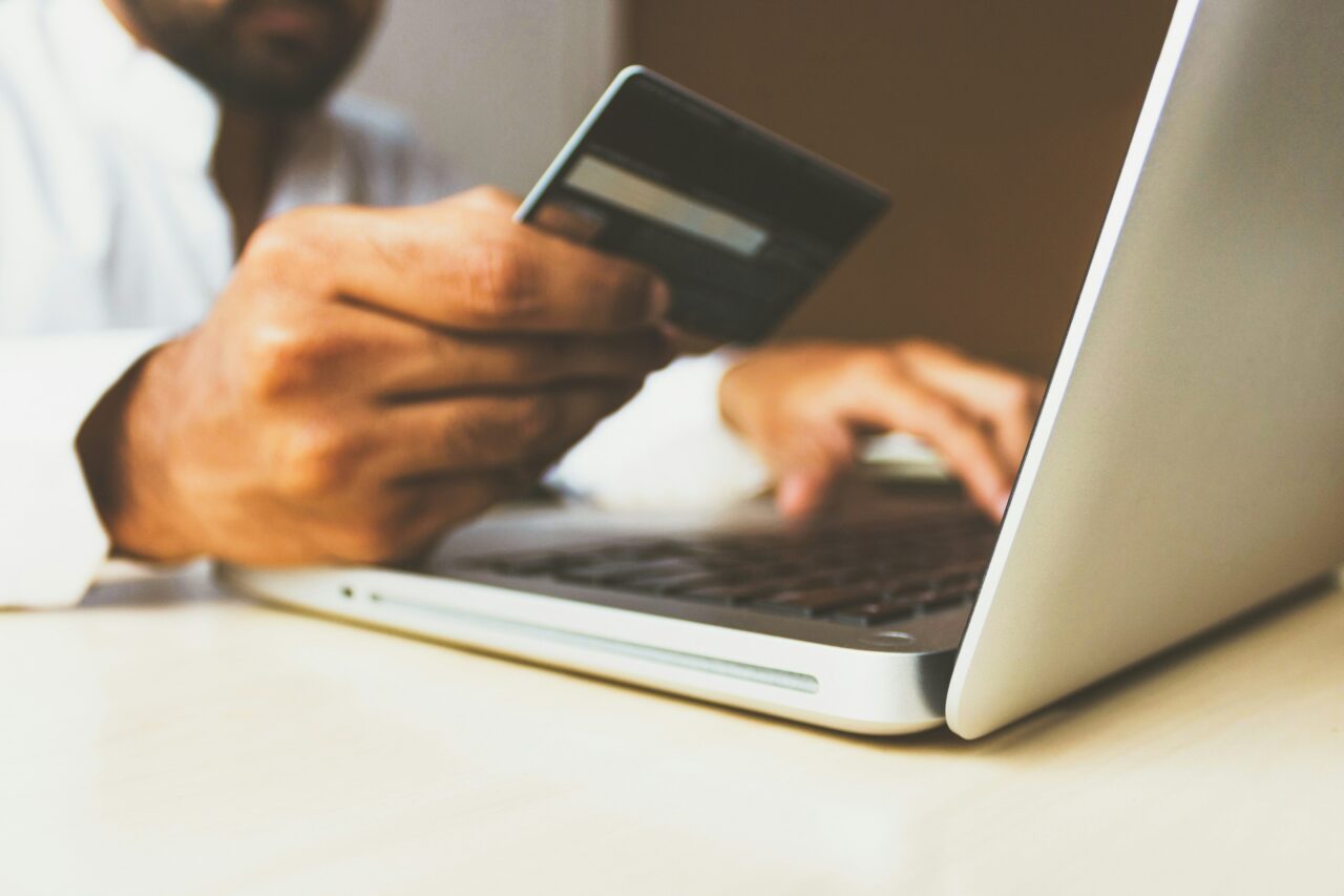 Osoba używająca laptopa i trzymająca kartę kredytową, by zachować anonimowość w sieci. Możliwe dokonywanie transakcji online.