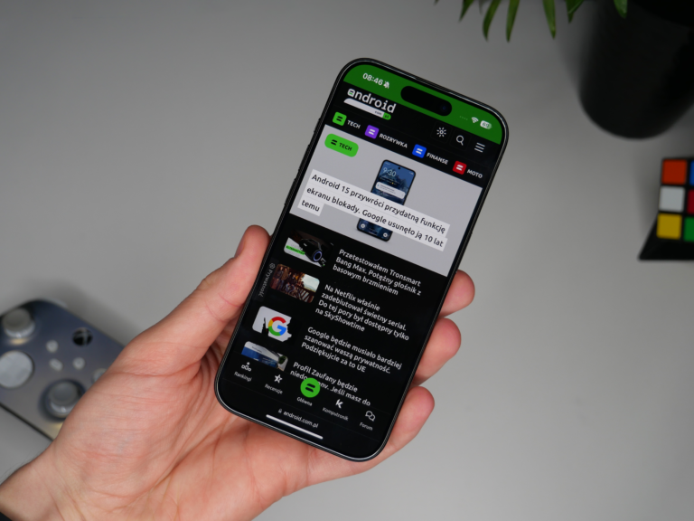 Osoba trzymająca apple iPhone 15 Pro wyświetlający stronę internetową z artykułami o tematyce Android, z widocznym logo serwisu i zielonym paskiem stanu u góry ekranu.