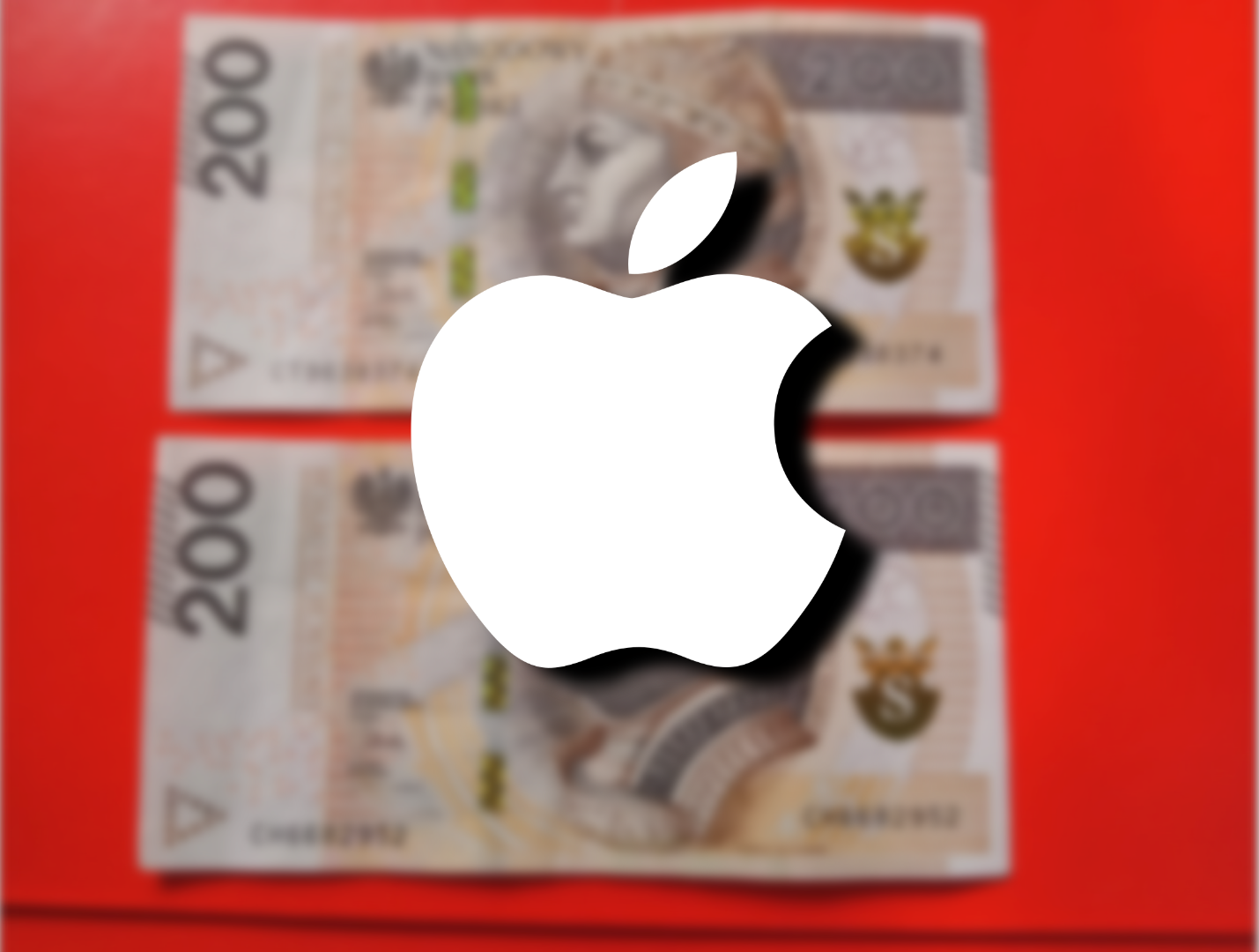 Dwa rozmyte banknoty o nominale 200 złotych leżące na czerwonym tle z białym logo Apple na pierwszym planie, które jest wyostrzone.
