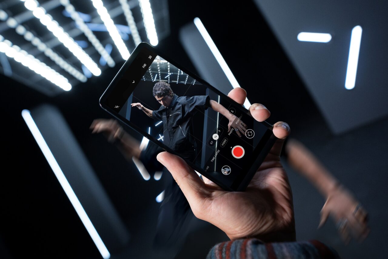 Osoba nagrywa smartfonem tancerza w ciemnym pomieszczeniu z jasnymi, poziomymi światłami w tle. Model ASUS ROG Phone 8