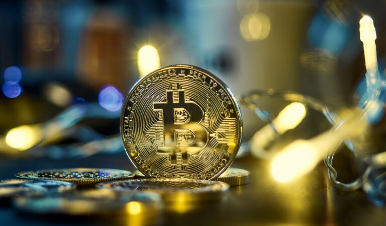 Złota moneta Bitcoin w ognisku na tle rozmytych świateł i innych monet.