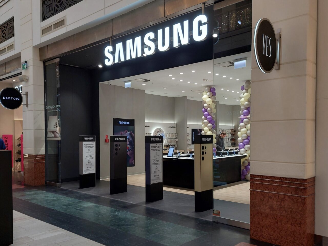 Wejście do salonu Samsung Store w CH Arkadia z reklamami produktów na stojakach przed sklepem i dekoracją z balonów.