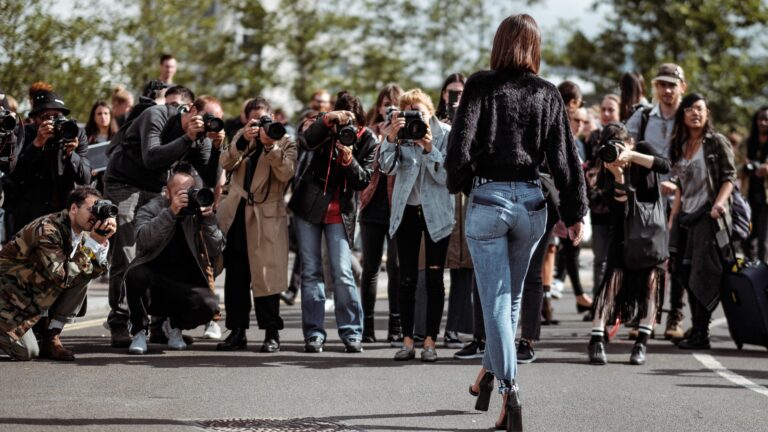 Kobieta idąca przed grupą fotografów robiących zdjęcia na ulicy.