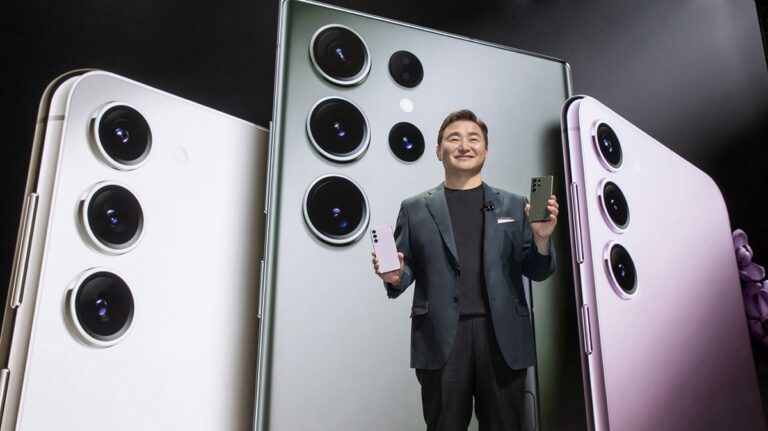 Mężczyzna stojący na scenie prezentuje dwa smartfony, w tle duże banery z powiększonymi obrazami tych telefonów. Samsung Galaxy Unpacked 2023 modele Galaxy S23