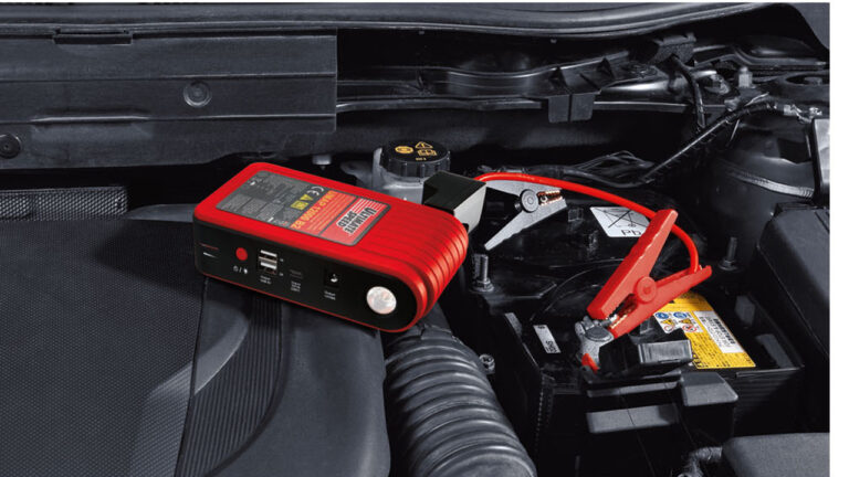 Czerwono-czarnay Powerbank do samochodu z Lidla podłączony do akumulatora samochodowego umieszczonego w komorze silnika.