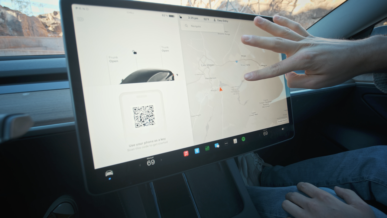 Osoba w środku samochodu dotyka ekranu dotykowego na desce rozdzielczej, wyświetlającego mapę nawigacyjną i różne funkcje pojazdu.