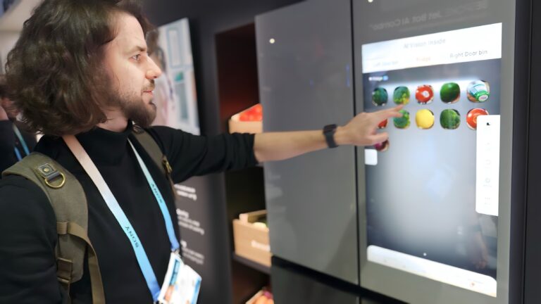 Mężczyzna dotyka ekranu interaktywnego. Inteligentna lodówka z wyświetlaczem. Na ekranie wyświetlają się ikony z owocami i warzywami.