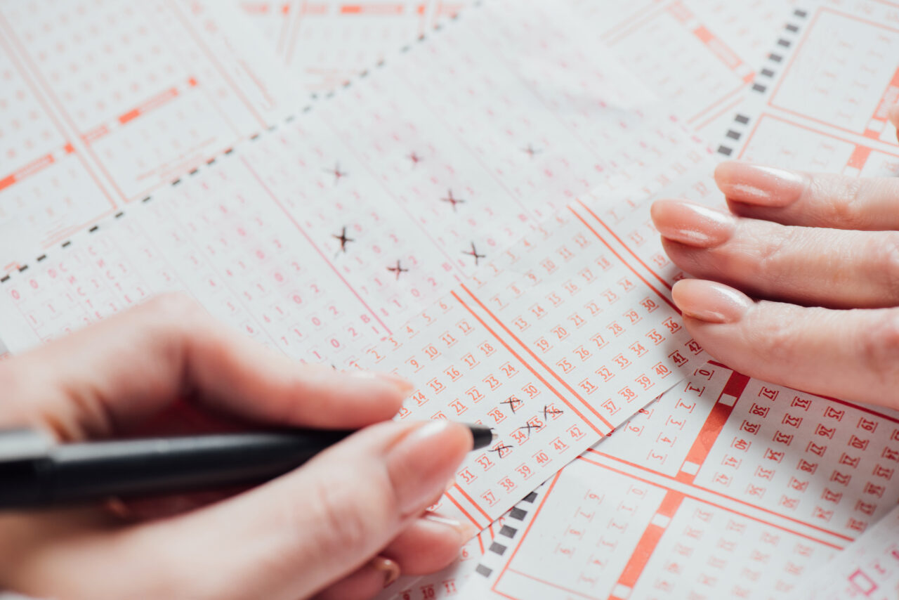Dłonie kobiety zaznaczające numery na papierowych kuponach loterii za pomocą długopisu.
