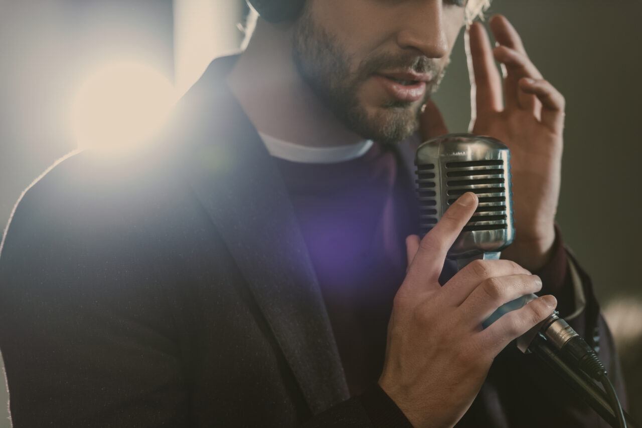 Mężczyzna śpiewający do retro mikrofonu z rozmytym tłem i światłem w tle.