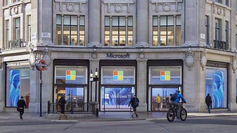 Wejście do sklepu Microsoft z logo firmy i reklamą Windows 11, obok wejścia do stacji metra, ludzie przechodzą obok, rowerzysta jedzie po drodze.