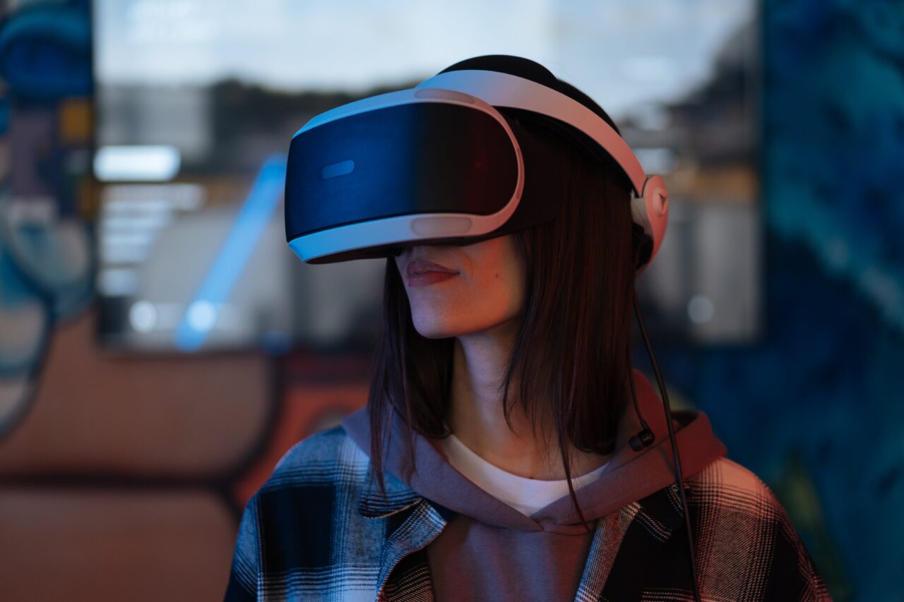 Kobieta nosząca gogle wirtualnej rzeczywistości stoi w pomieszczeniu o oświetleniu typu ambient. Obraz ilustrujący tekst o temacie: wirtualny gwałt w Metaverse.
