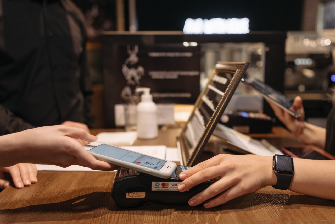 Klientka dokonuje płatności zbliżeniowej smartfonem na terminalu płatniczym w sklepie.