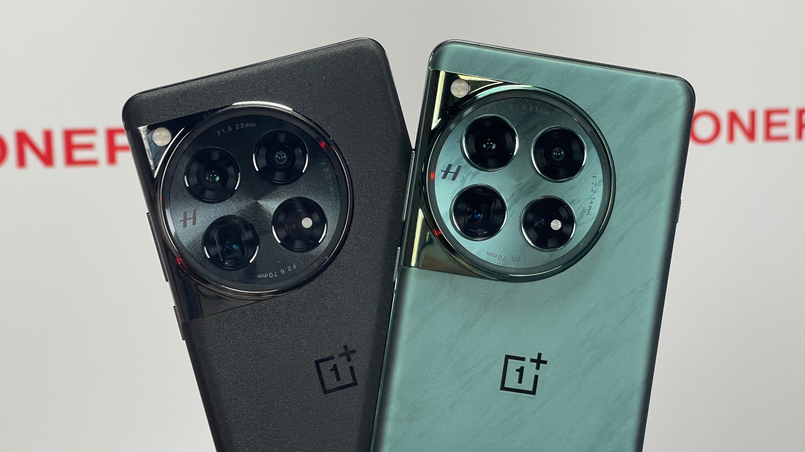 Dwa smartfony OnePlus z wystającymi modułami aparatów fotograficznych na tle z logotypem firmy.