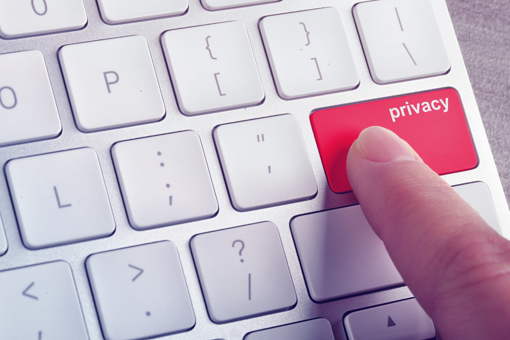 Klawiatura komputera z czerwonym klawiszem z napisem "privacy", którego dotyka palec osoby.
