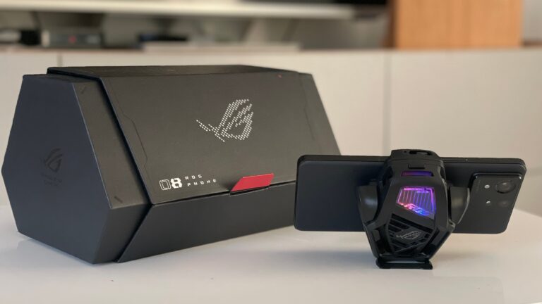 Czarny gamingowy smartfon z załączonym wentylatorem chłodzącym, oparty o pudełko z logo i napisem "ROG PHONE".