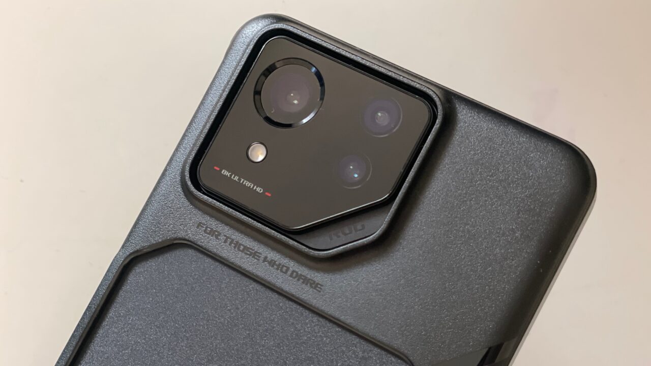 Część tylna smartfona z widocznym czarnym modułem aparatu fotograficznego z trzema obiektywami i lampą błyskową, umieszczonym na teksturowanej obudowie z napisami.