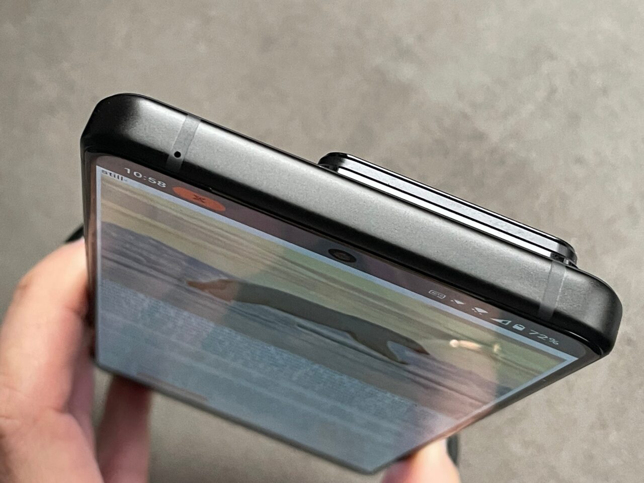 Skladany smartfon trzymany w ręce z widocznym przednim aparatem i wyświetlaczem pokazującym część interfejsu użytkownika.