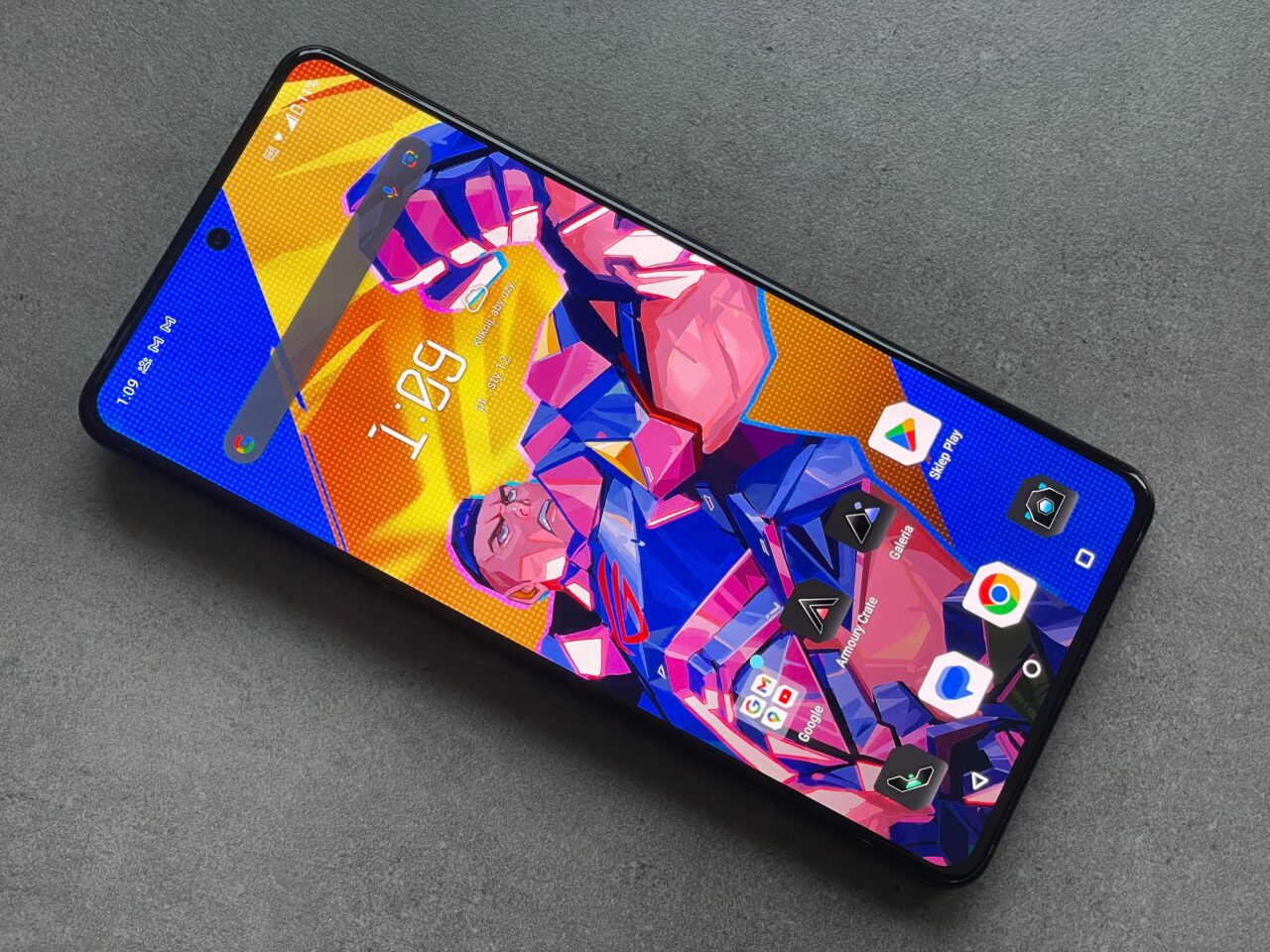 Smartfon leżący na szarym tle z kolorową tapetą przedstawiającą postać komiksową na ekranie głównym.