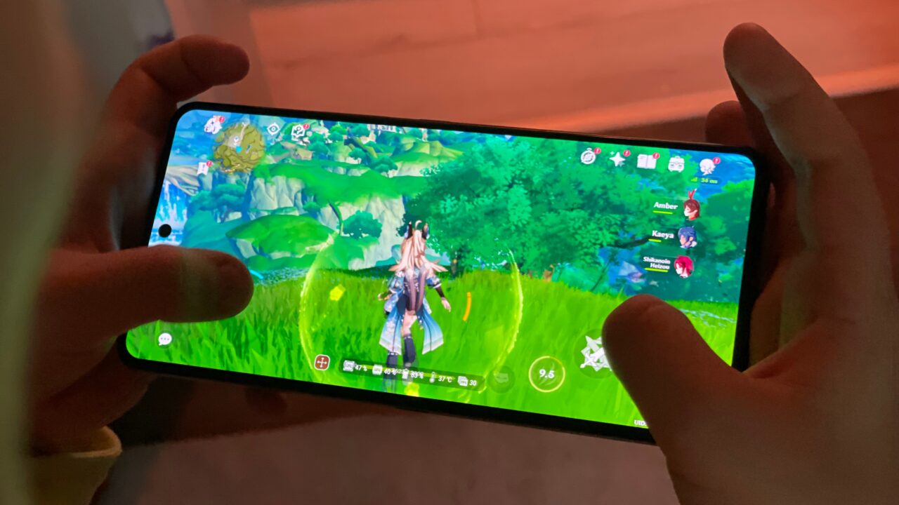 Osoba trzymająca smartfon, na którym wyświetlana jest gra z bohaterem stojącym na zielonej trawie w wirtualnym świecie.