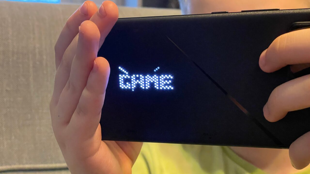 Osoba trzymająca smartfon wyświetlający słowo "GAME" za pomocą migających białych diod LED.