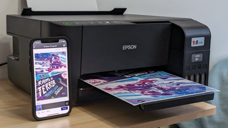 Drukarka atramentowa Epson na biurku wydrukowała kolorową grafikę, obok niej smartphone z otwartą aplikacją drukowania.