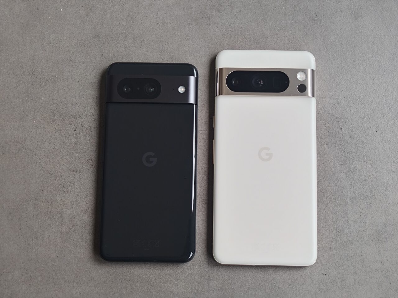 Dwa smartfony Google Pixel leżące tyłem na szarym tle; jeden czarny, a drugi biały.