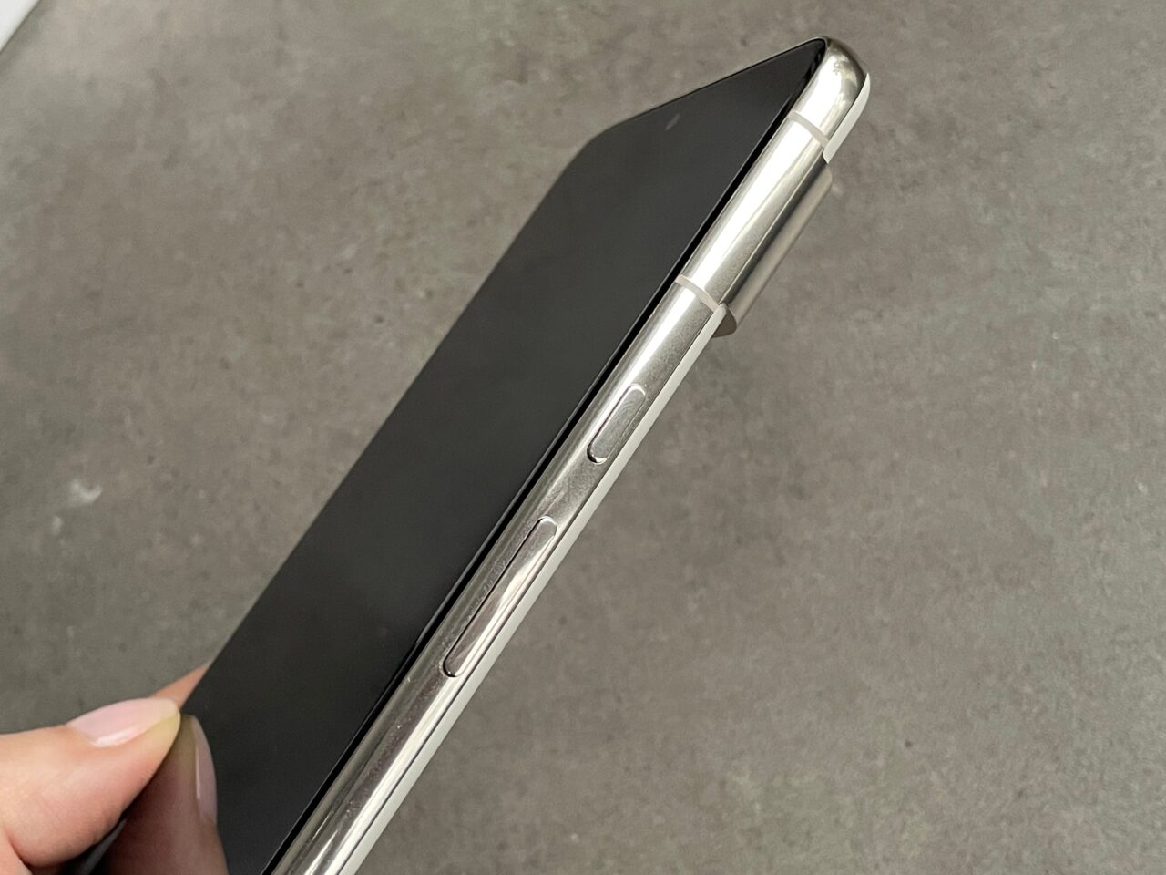 Czarny smartfon trzymany w dłoni, przedstawiony ukośnie z bocznym widokiem na przyciski głośności i przełącznik trybu wyciszenia.