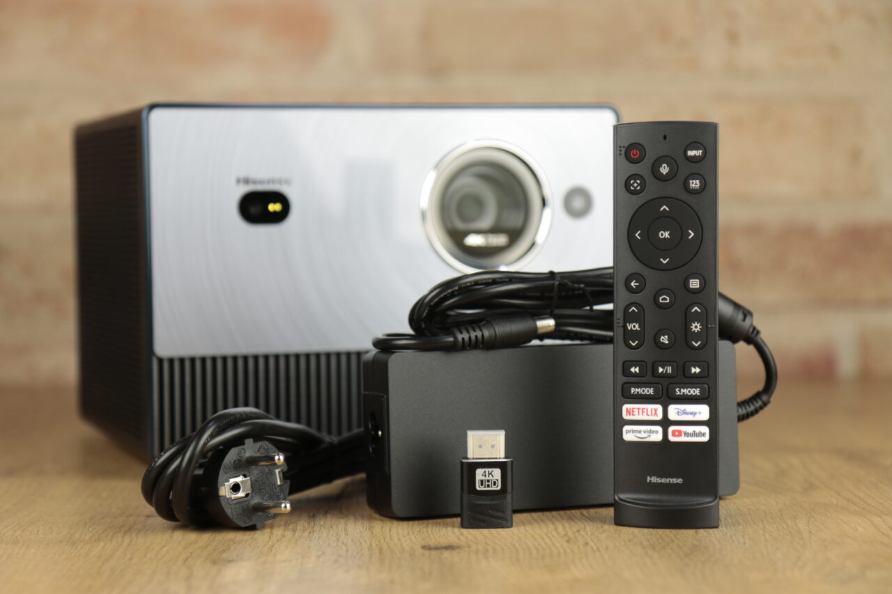 Zestaw sprzedażowy recenzowanego projektora Hisense C1 z widocznymi zasilaczem, pilotem i przejściówką HDMI