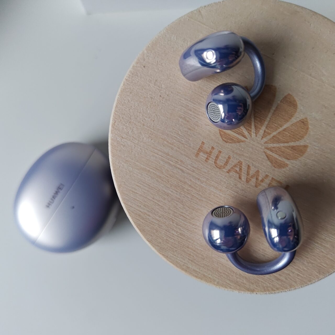 Słuchawki bezprzewodowe marki Huawei i futerał ładujący umieszczone na drewnianej okrągłej podstawce z logo firmy.