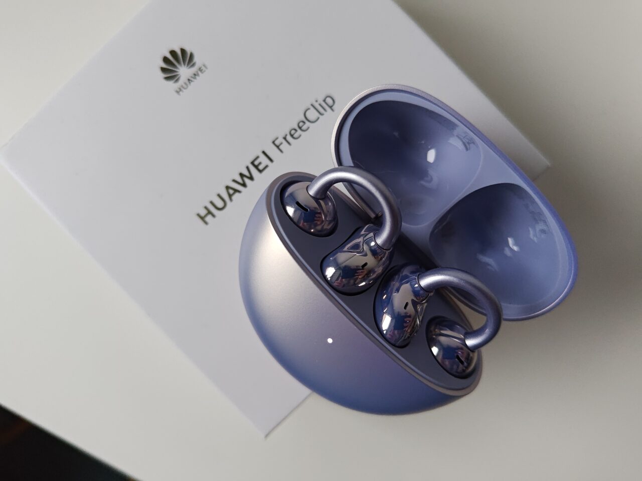 Słuchawki Bluetooth marki Huawei FreeClip w otwartym, niebieskim etui leżące na białym pudełku z logotypem producenta.