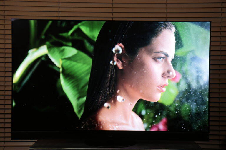 Telewizor recenzja Panasonic 65MZ2000 wyświetlający zdjęcie profilowe kobiety, która patrzy w dal, z kroplami wody na jej twarzy i tle roślinnym.