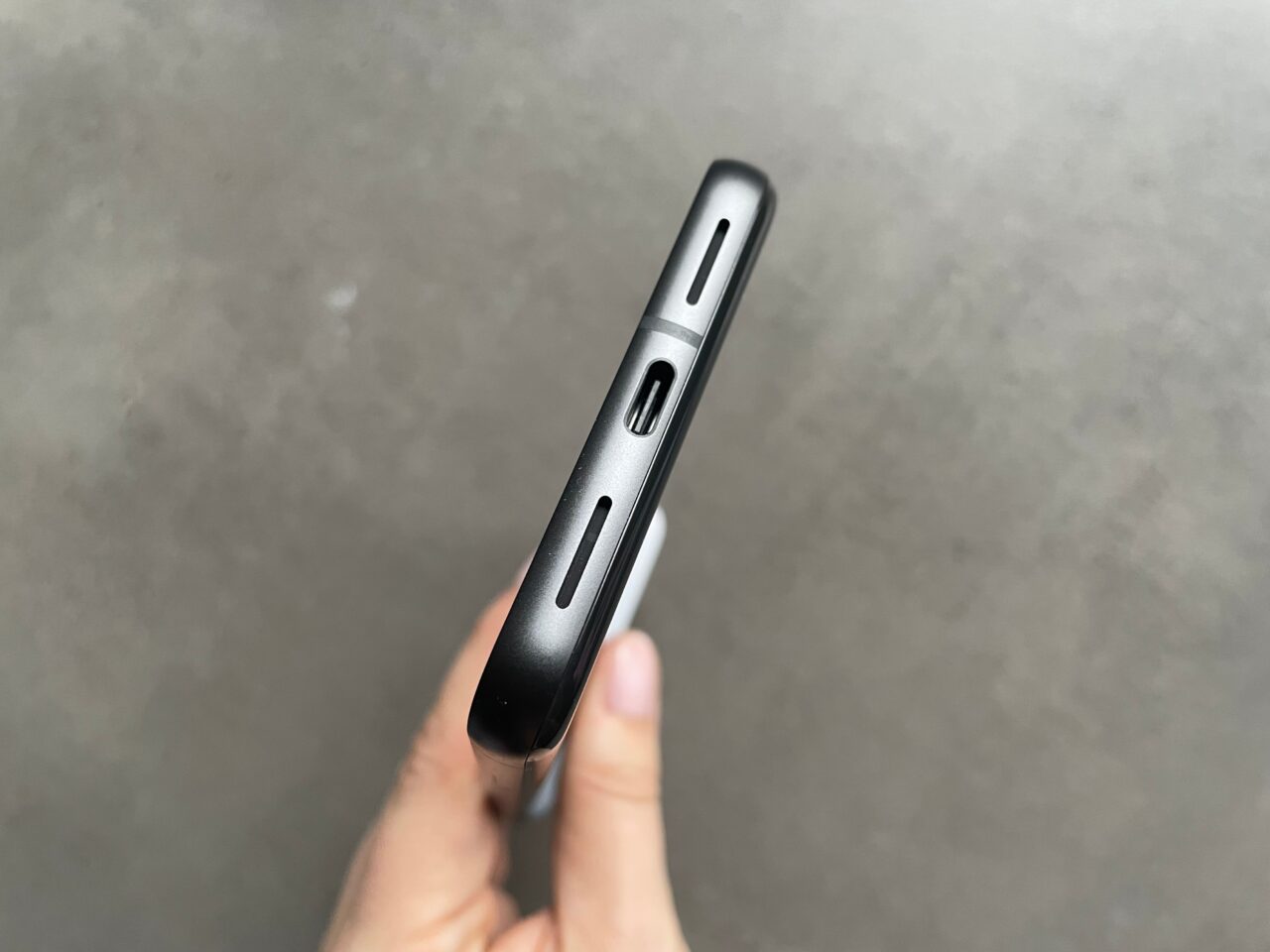 Czarny smartfon trzymany w dłoni z boku, pokazujący przyciski głośności, slot karty SIM i przycisk blokady.