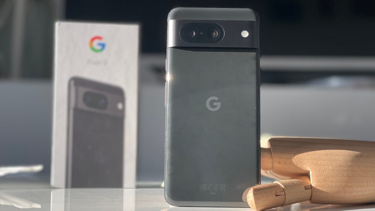 Smartfon Google Pixel w czarnym kolorze z tyłu, oparty o drewnianą figurkę z rozmytym pudełkiem na tle.