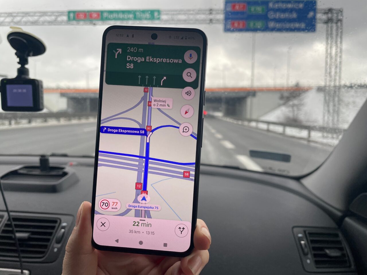 Smartfon trzymany w ręce na tle przedniej szyby samochodu, wyświetlający aplikację nawigacyjną z mapą, wskazującą trasę na drodze ekspresowej S8.