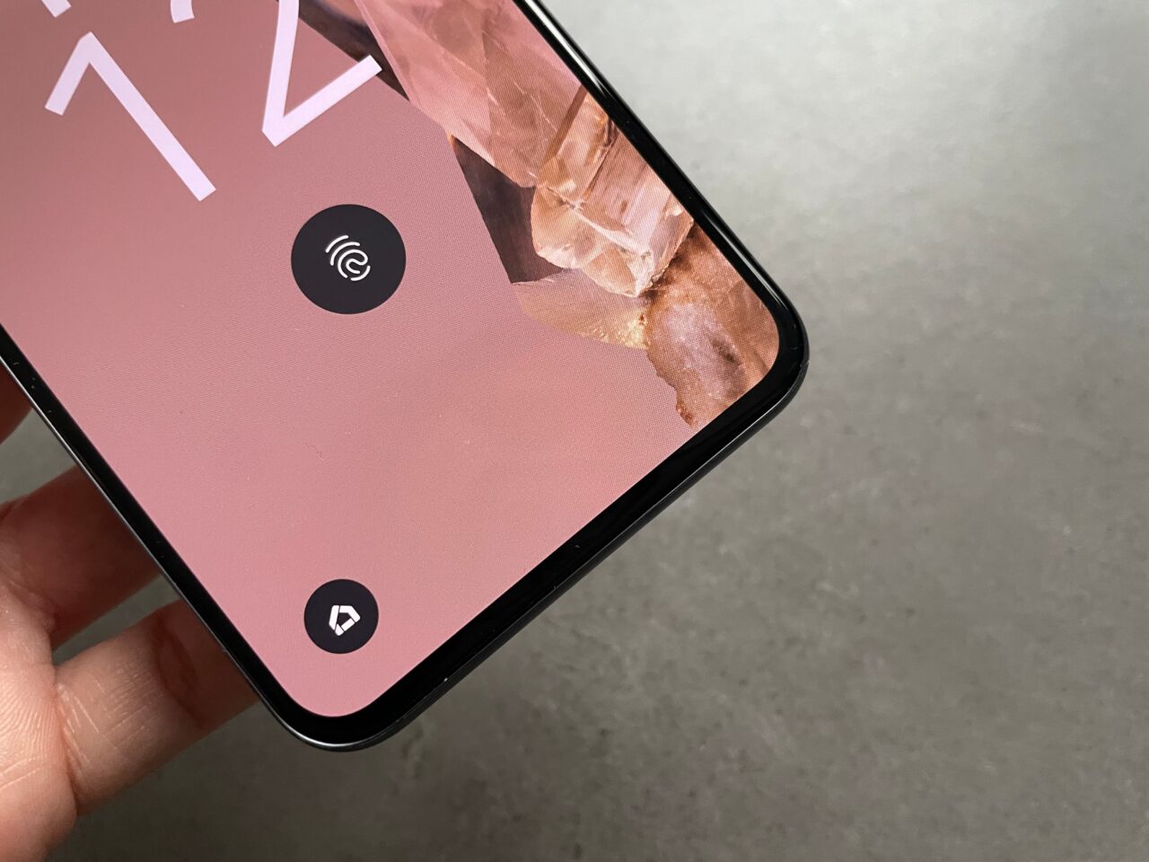 Ekran smartfona z graficznym tłem i widocznym symbolem odcisku palca, trzymany w dłoni na szarym tle.