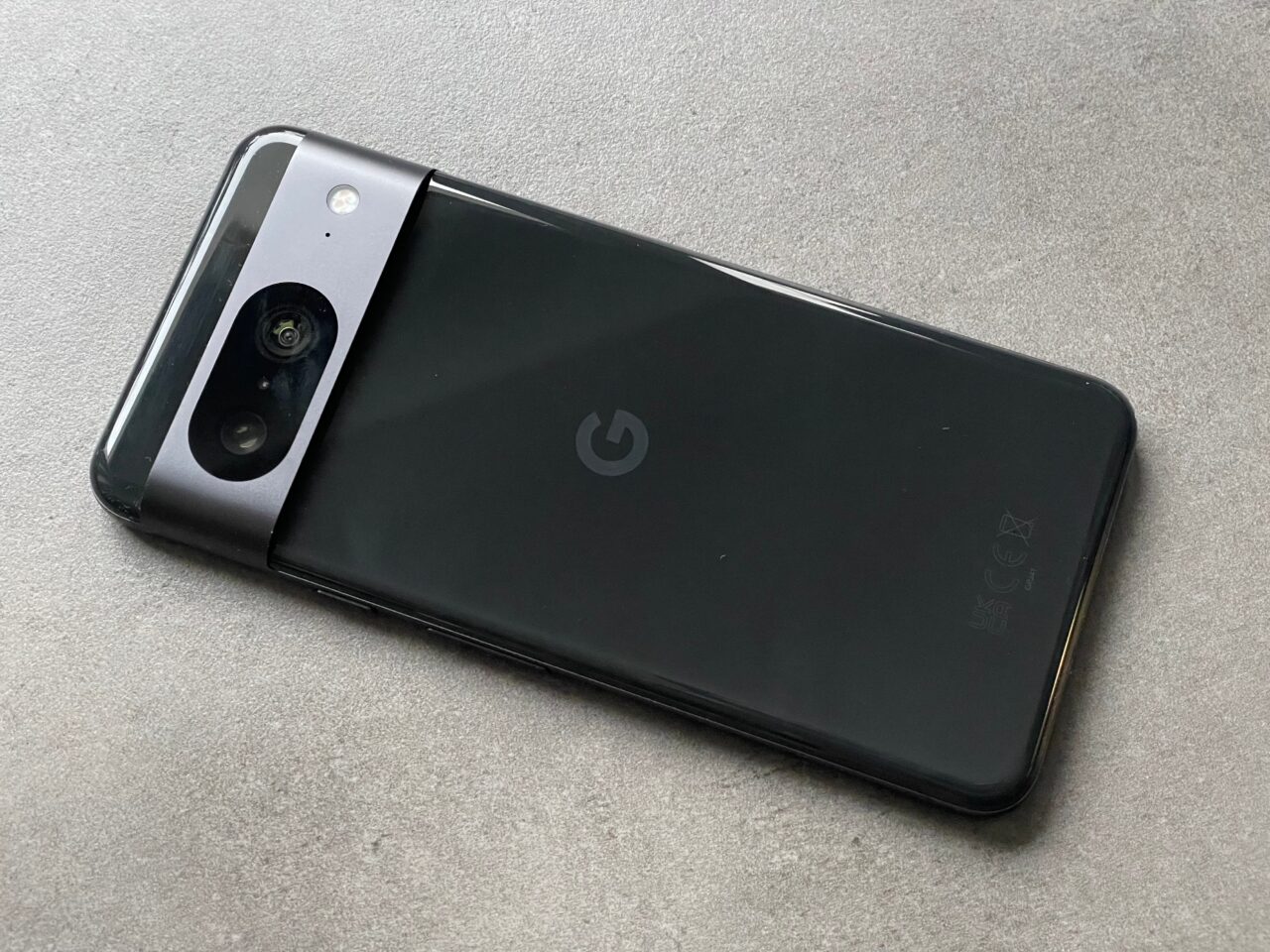 Czarny smartfon z tylnym aparatem fotograficznym umieszczonym w górnym rogu i logo producenta pośrodku tylnej obudowy, leżący na szarym tle.