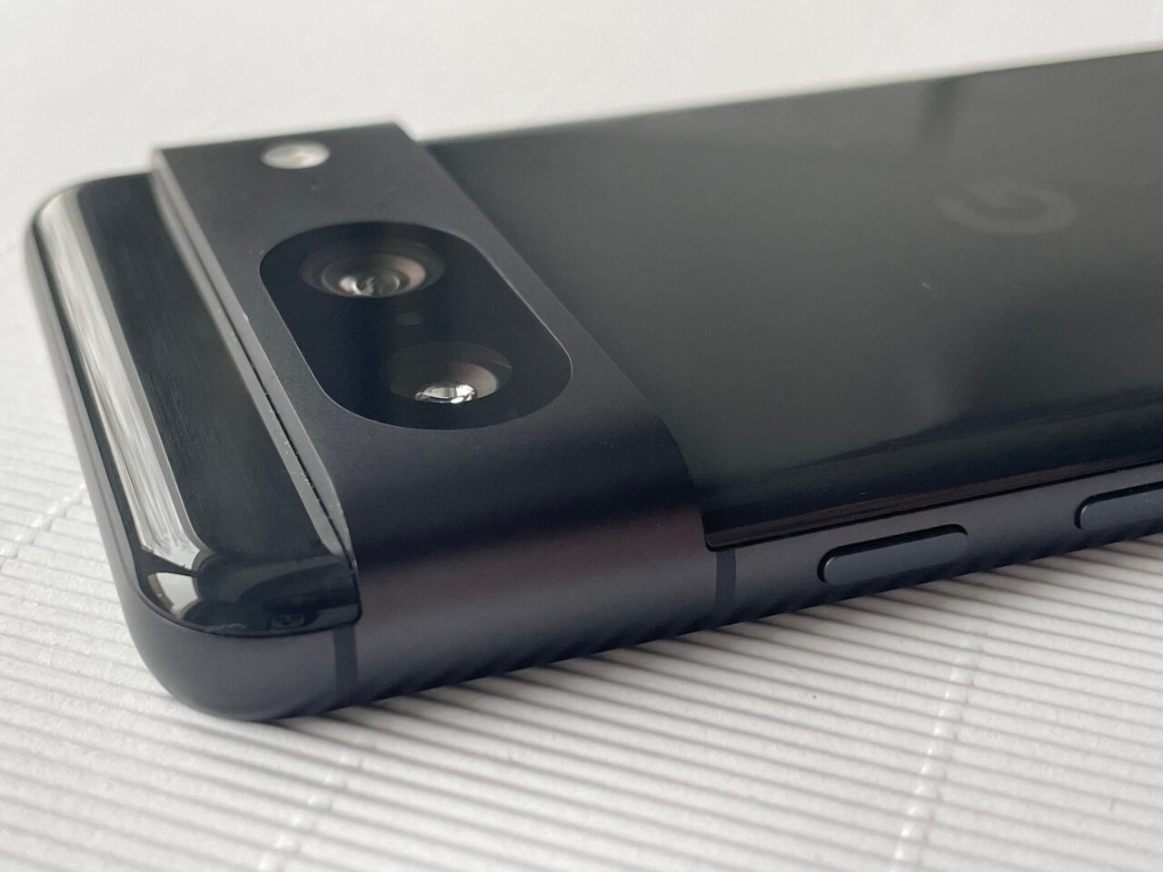 Smartfon leżący na białej powierzchni z szczegółowym widokiem na tylny aparat fotograficzny i przyciski boczne.