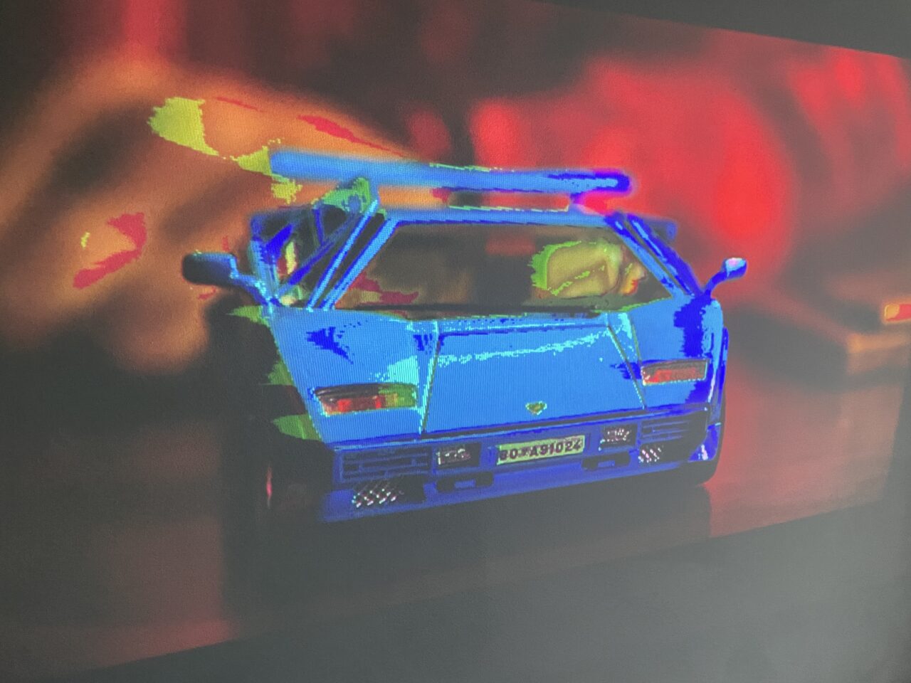Zdjęcie modelu samochodu w niebieskim kolorze z efektem termowizji na tle z czerwonymi i czarnymi plamami.