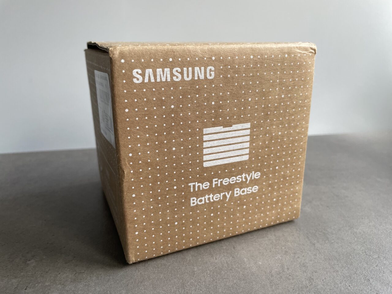 Brązowe kartonowe opakowanie z napisem "SAMSUNG The Freestyle Battery Base" stoi na szarym tle.