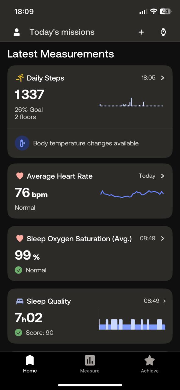 Zrzut ekranu aplikacji zdrowotnej prezentujący najnowsze pomiary aktywności fizycznej i stanu zdrowia: kroki dziennie (1337 kroków, 26% celu, 2 piętra), zmiany temperatury ciała, średnia tętno (76 bpm), średnie nasycenie tlenem w czasie snu (99%), oraz jakość snu (7 godzin 2 minuty, wynik 90). Na dole interfejsu znajdują się przyciski nawigacyjne.