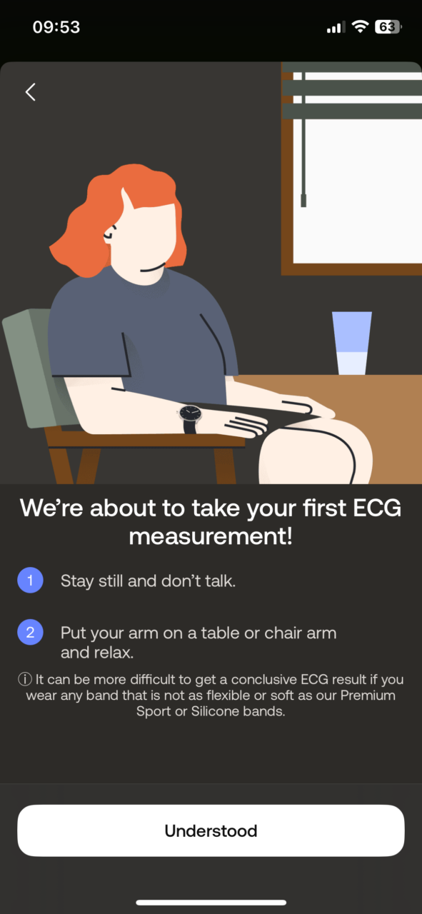 Postać siedząca przy stole gotowa do wykonania pomiaru EKG z zegarkiem na nadgarstku, przed nią na ekranie wyświetlają się instrukcje przygotowawcze i przycisk "Zrozumiałem/Zrozumiała".