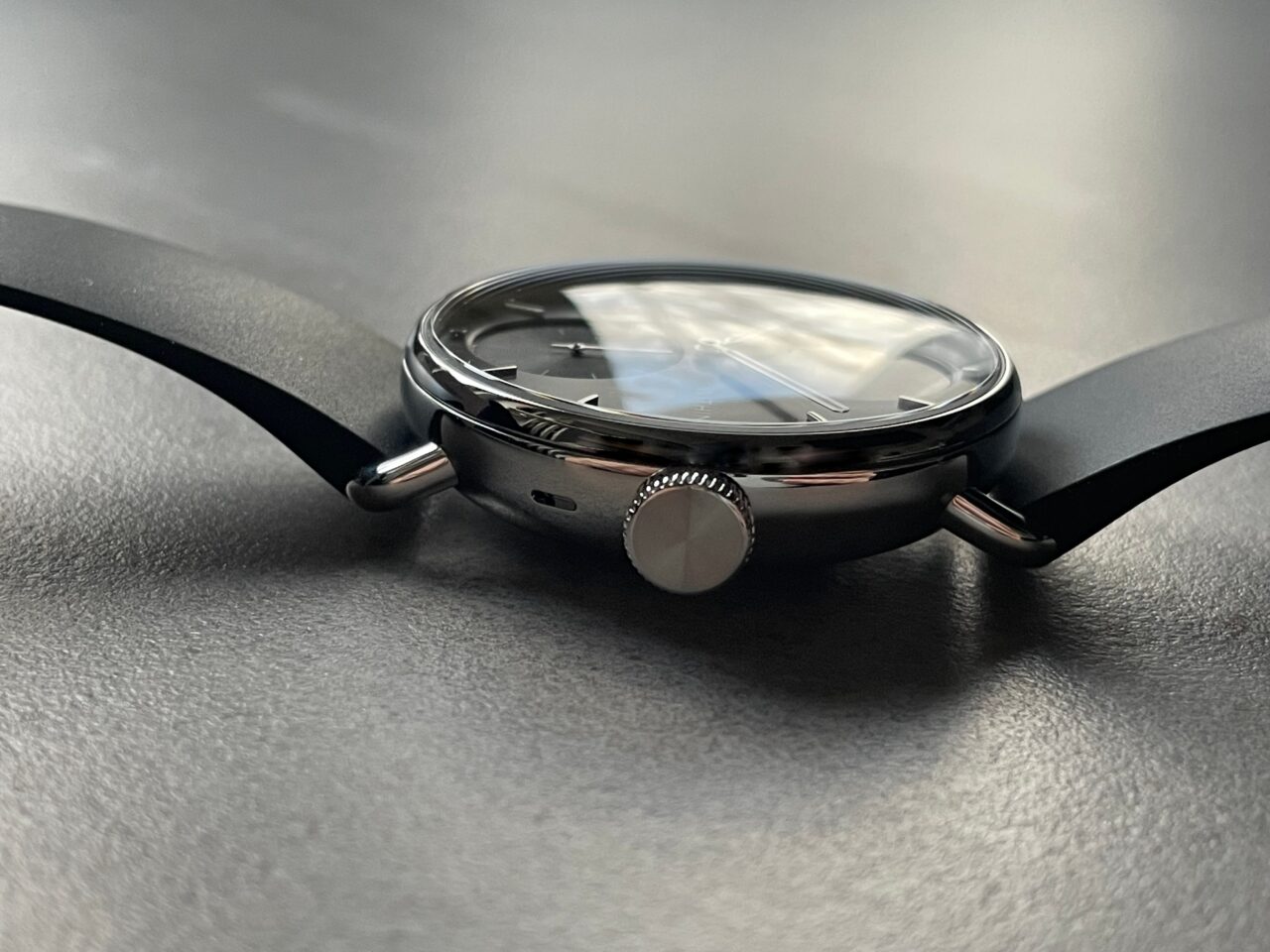 Zegarek na czarnym pasku z chromowaną obudową i wypukłym szkłem, położony na matowym podłożu.