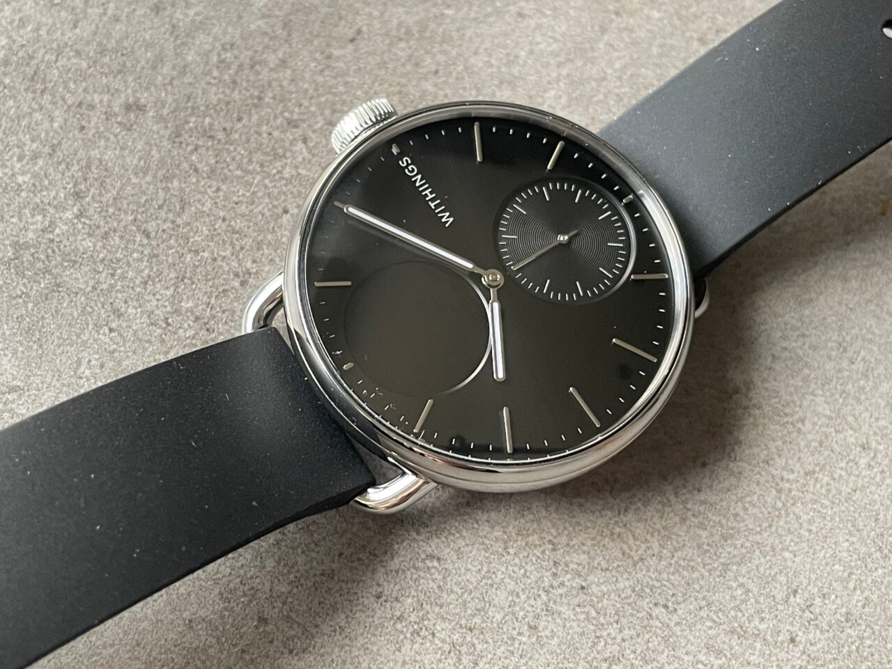 Elegancki zegarek na czarnym pasku z czarną tarczą, białymi indeksami i dodatkowym małym cyferblatem.