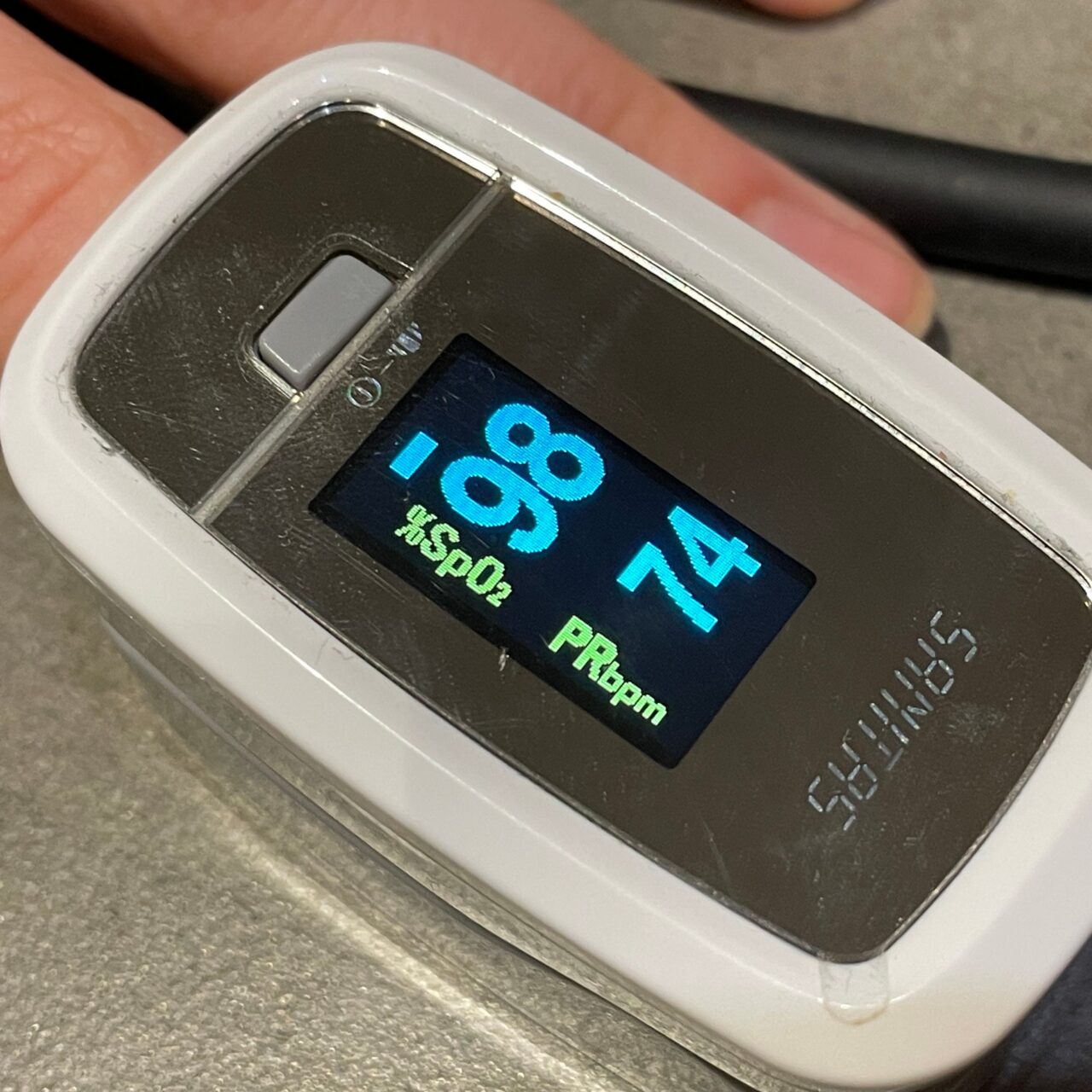 Pulsoksymetr na palcu z wyświetlaczem wskazującym poziom nasycenia krwi tlenem (SpO2) na poziomie 98% oraz tętno (PRbpm) wynoszące 163 uderzenia na minutę.