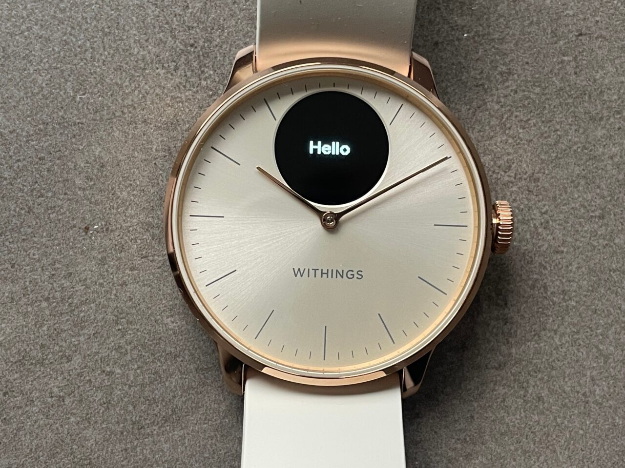 Zegarek Withings z różowozłotą kopertą i białym paskiem, cyferblat z napisem "Hello".