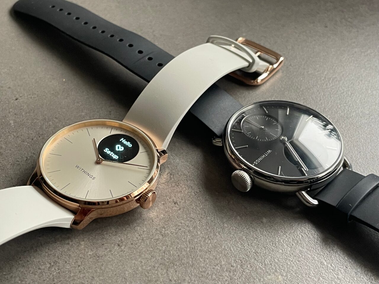 Dwa zegarki na szarym tle, jeden z miedzianą kopertą i białą tarczą z subcyferblatem powiadomień, drugi czarny z dodatkowym małym tarczą zegarową.
