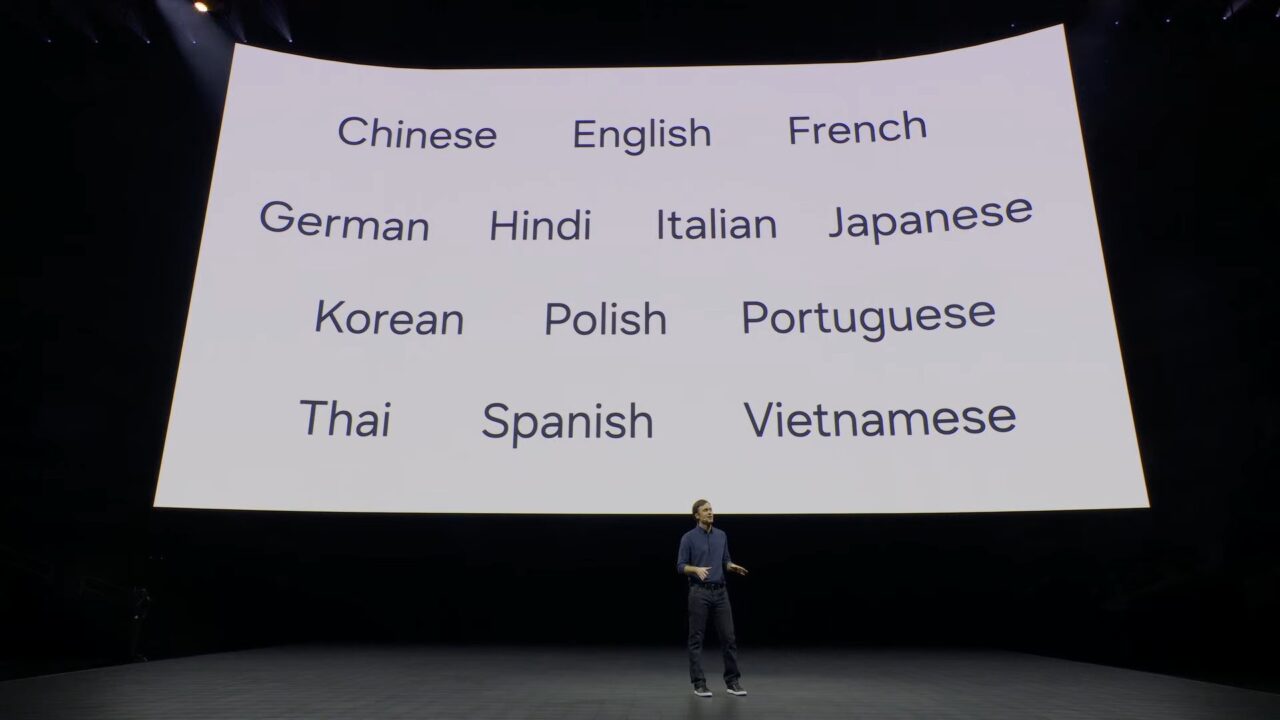 Prelegent stoi na scenie Samsung przed dużym ekranem, na którym wyświetlona jest lista nazw języków, w tym chiński, angielski, francuski, niemiecki, hindi, włoski, japoński, koreański, polski, portugalski, tajski, hiszpański i wietnamski.