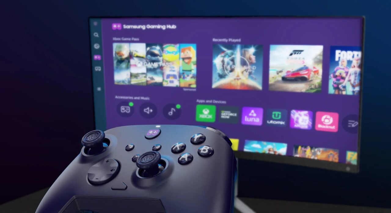 Pad do gier na pierwszym planie z rozmytym tłem przedstawiającym ekran telewizora z menu Samsung Gaming Hub i widocznymi ikonami aplikacji oraz grami wideo.