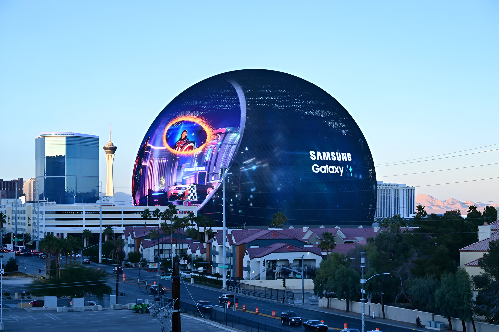 Zdjęcie współczesnej panoramy miejskiej z dominującym sferycznym budynkiem z reklamą Samsung Galaxy, w tle widoczne są góry i wieża obserwacyjna.